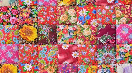 A imagem é uma foto. Vários pedaços de tecidos diferentes, de cores e estampas diversas, formam uma colcha.