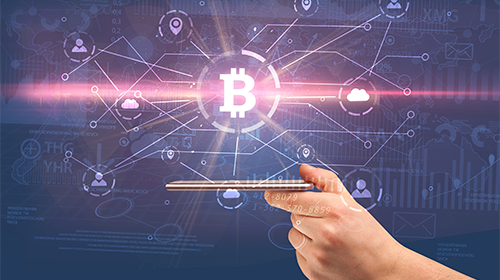 A imagem é uma montagem com foto e ilustrações, em um fundo azul. Uma mão segura um celular com a tela virada para cima. Acima da tela, está o símbolo de bitcoin, a letra B no centro de um círculo. Outros ícones estão ligados ao símbolo por linhas, entre eles nuvem, localização e pessoa.